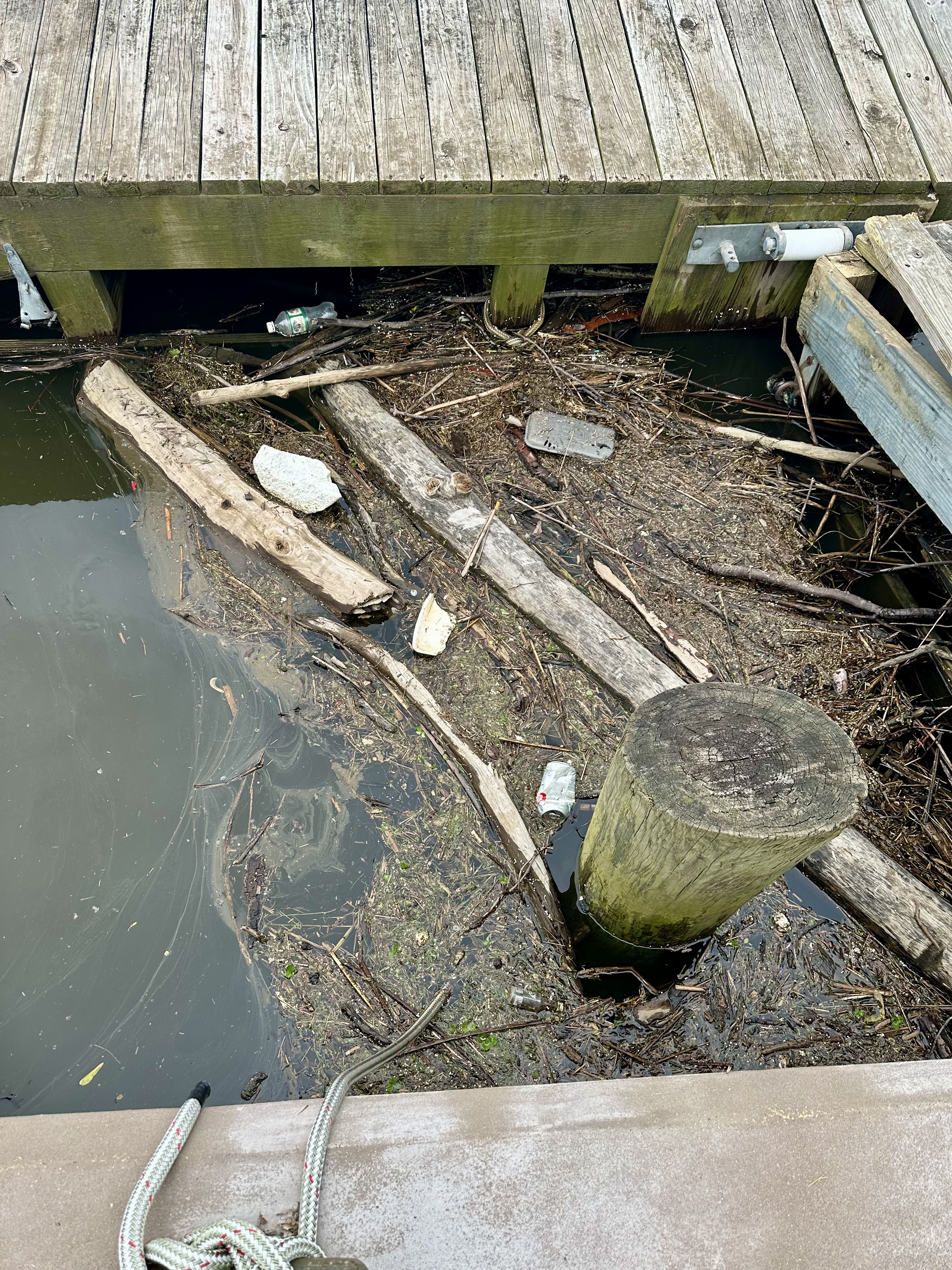 Debris packed under dock pilings on the Connecticut River — branches, plastic, and trash accumulating in locations unreachable from shore